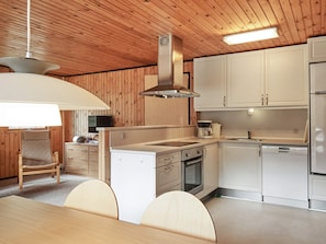 A modern kitchen with wooden paneling, white cabinetry, a built-in oven, and a dining area with a table and chairs.