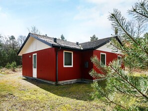 En rød træhytte med skråt tag, en lille veranda og et vindue.