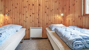A room with wooden walls, two beds with blue bedding, a wall-mounted heater, and a window on the right. - 6 Person Holiday Home in Aakirkeby (Akirkeby)