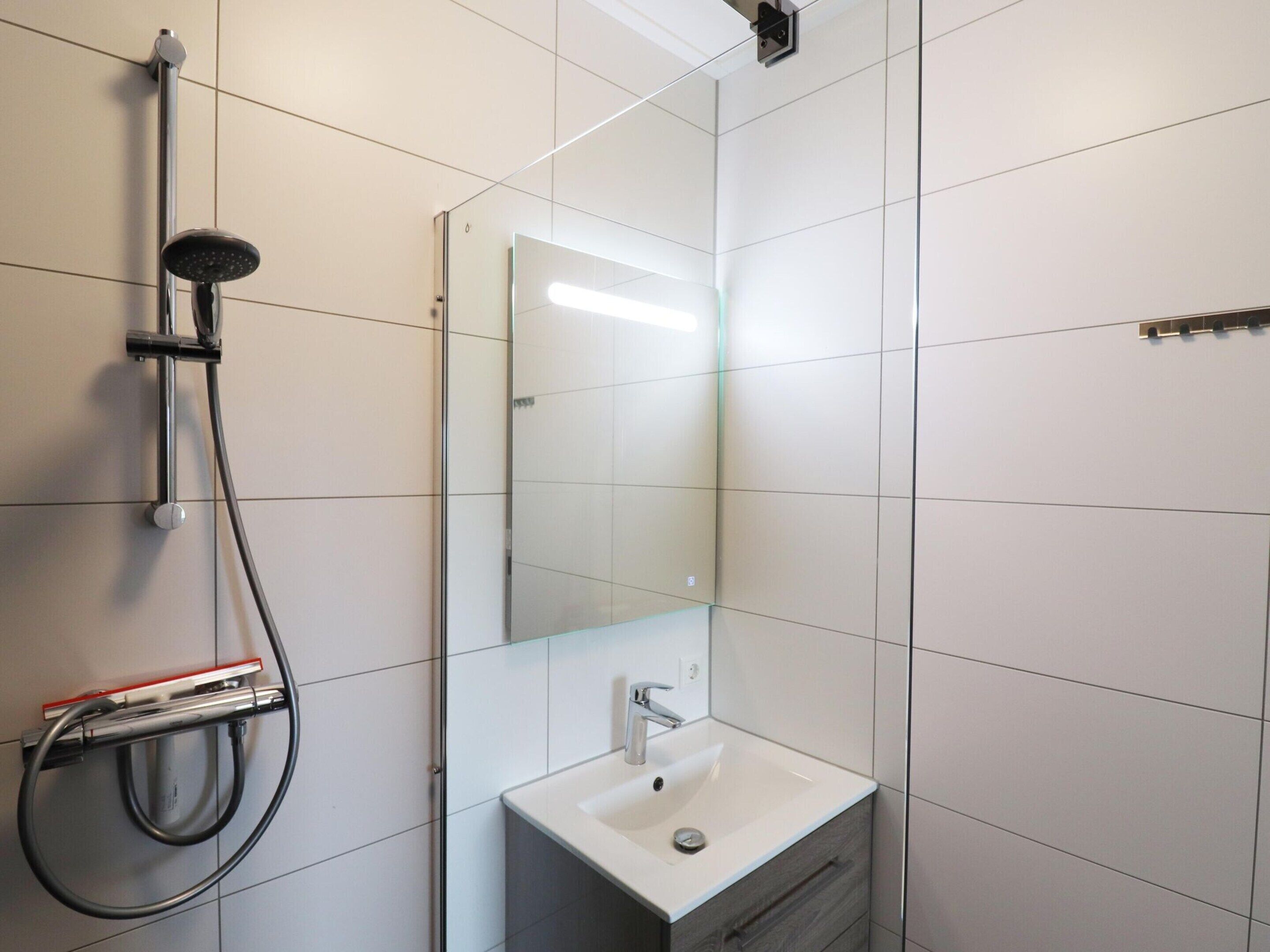 Un bagno moderno con cabina doccia in vetro, un lavabo bianco e uno specchio.
