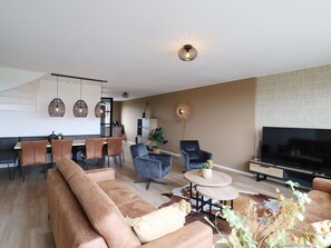 A modern living room with a sofa, a TV, and a dining area with chairs and a table.