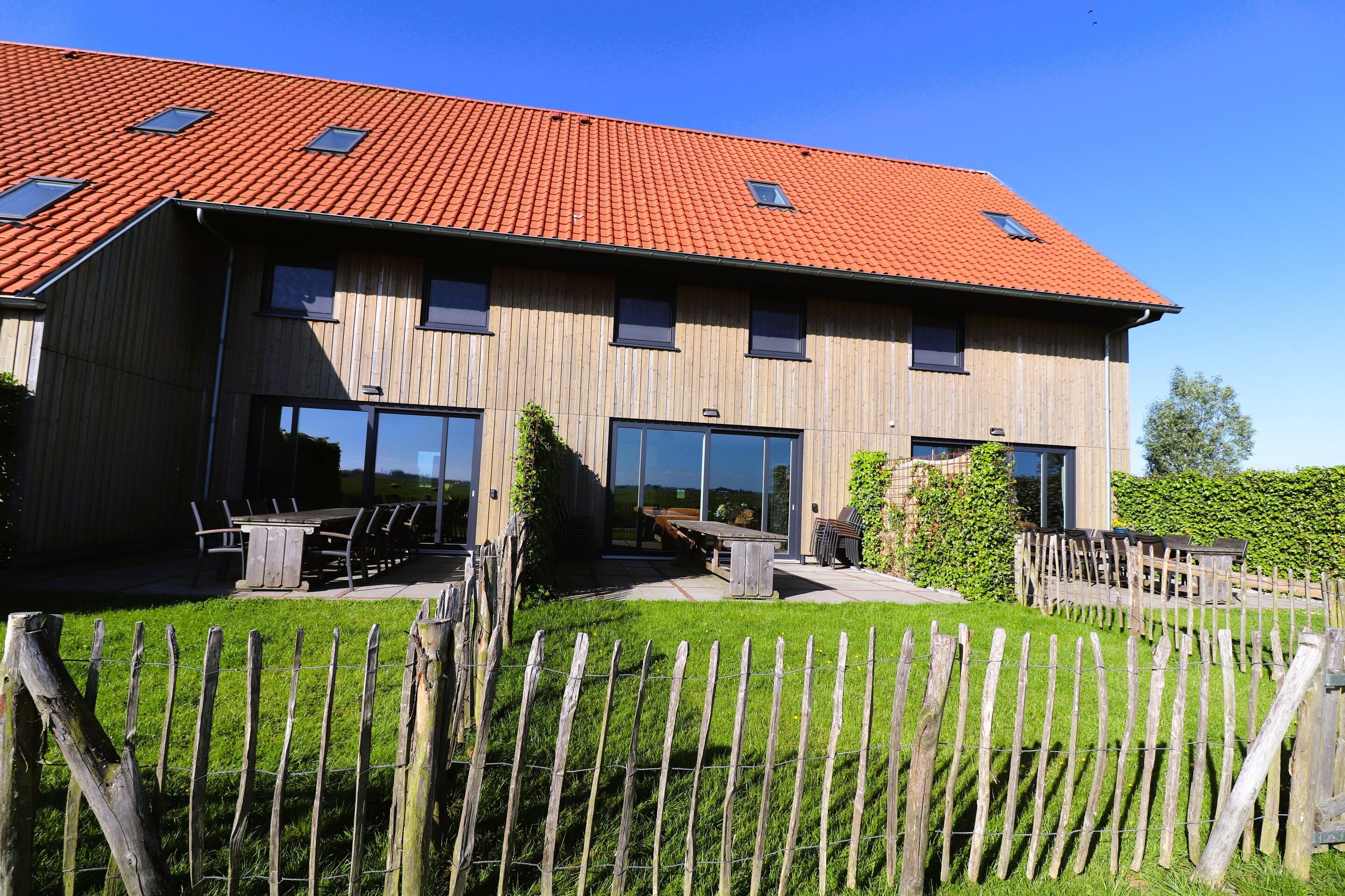 A two-story wooden building with a red-tiled roof, large windows, and a fenced outdoor area.