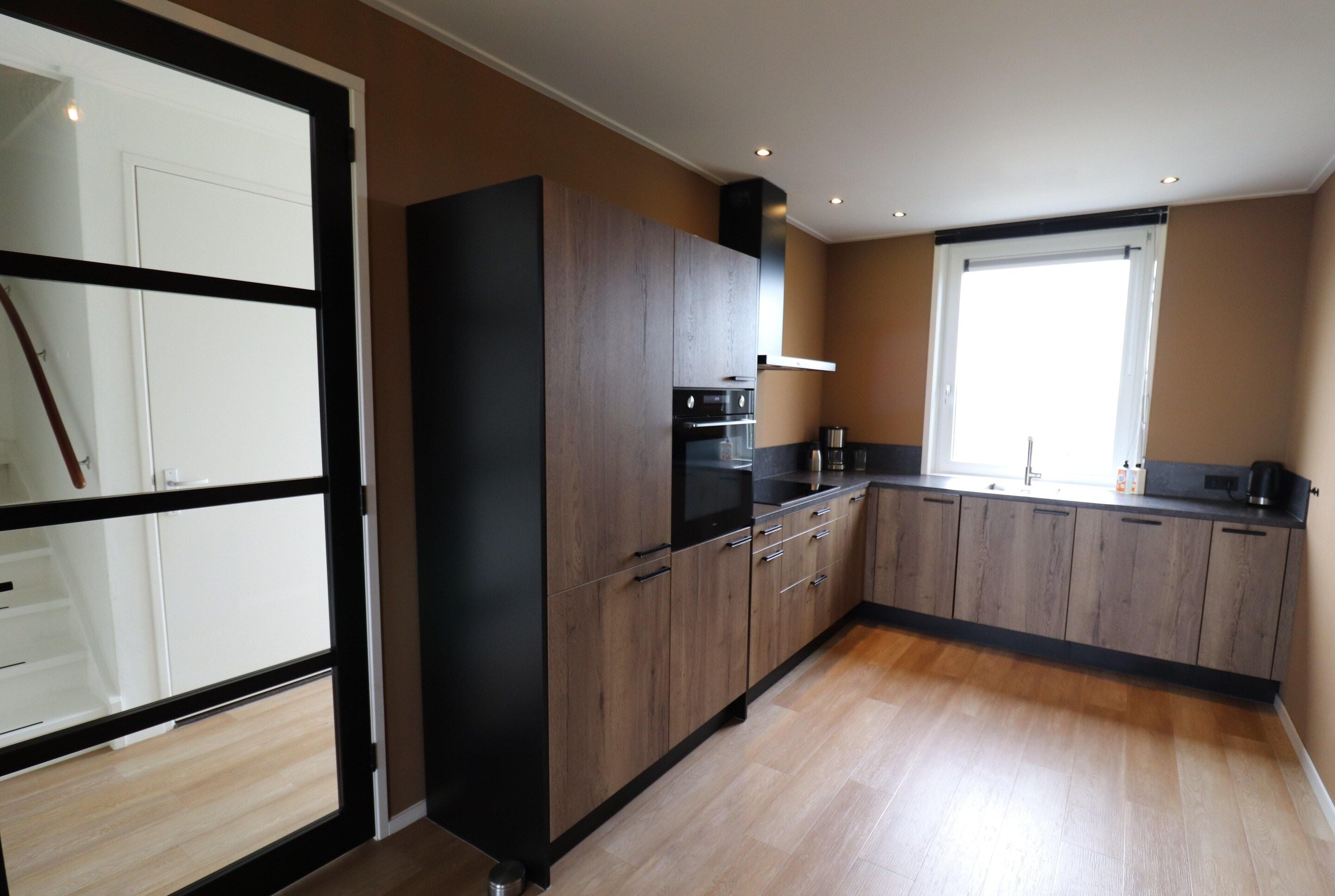 Eine moderne Küche mit Holzausstattung, einem schwarzen Kühlschrank und einem Fenster für natürliches Licht.