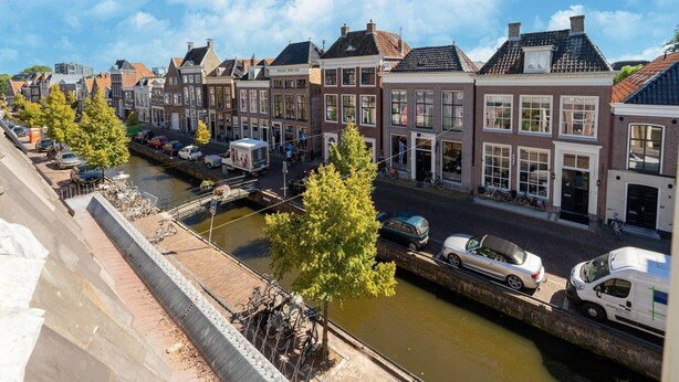 A canal-side street with traditional European buildings, a bridge, and parked cars. - 2 Adjacent Apartments in the Heart of Sneek (Sneek)