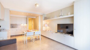 A modern kitchen with white cabinets, a dining table with chairs, a TV, and a small sailboat decoration. - Apartment by Belgian Coast With Beach Views (Koksijde)