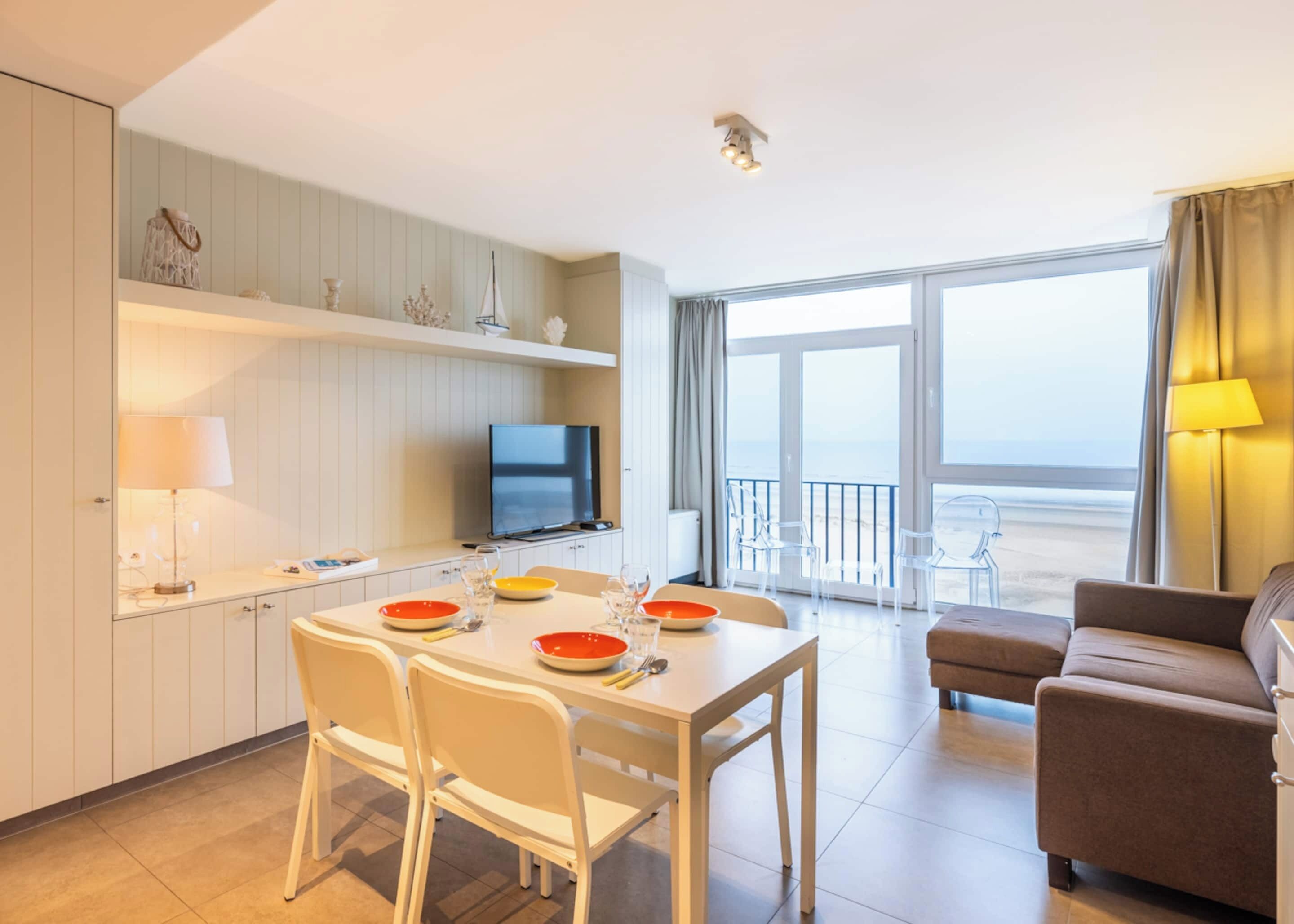 Una camera d'albergo moderna con zona pranzo, TV, balcone e vista, e divano.