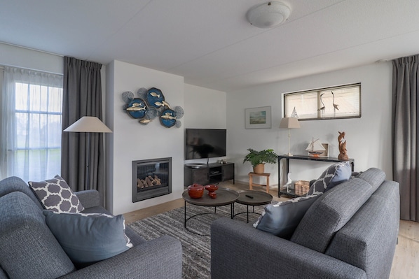 A modern living room with grey sofas, a flat-screen TV, a fireplace, and decorative wall art.