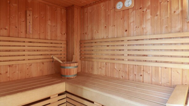 Una sauna in legno con panche, un catino di legno e due orologi a parete.