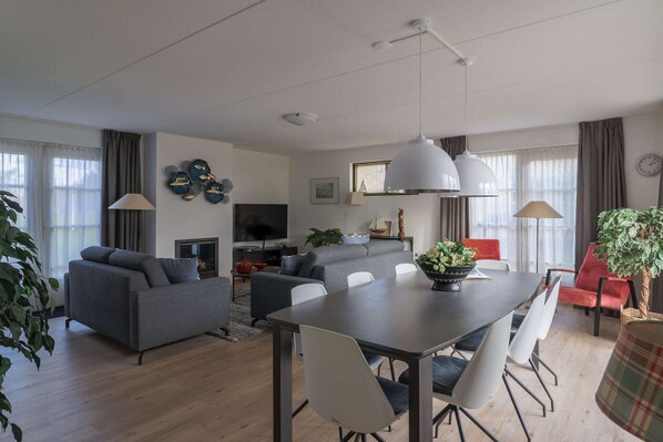 A modern living room with a sofa, dining table, chairs, a TV, and decorative items. - Spacious Villa in a Holiday Park in Makkum (Makkum)