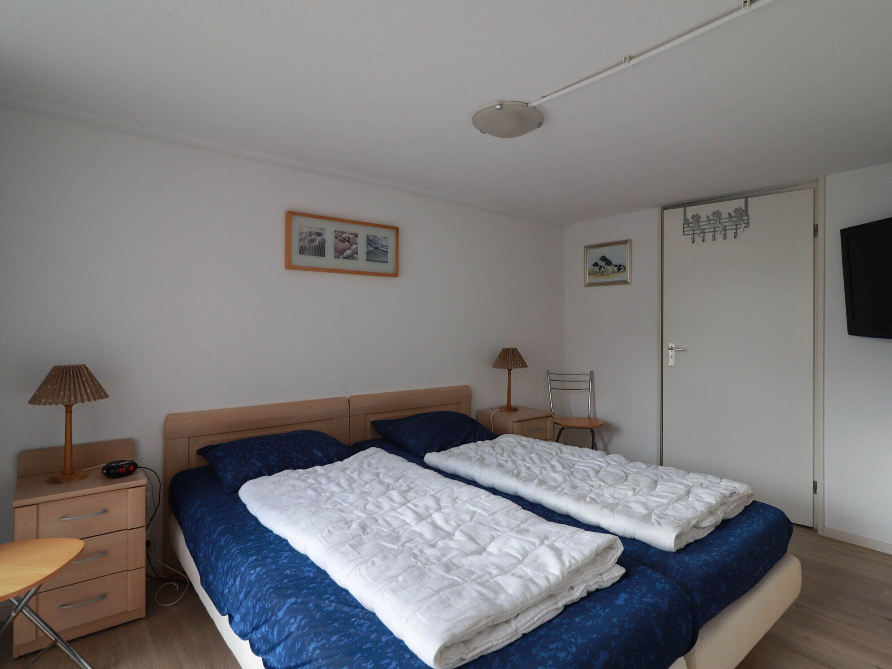 Une chambre avec deux lits, une table de chevet, une lampe, une chaise et un téléviseur fixé au mur.