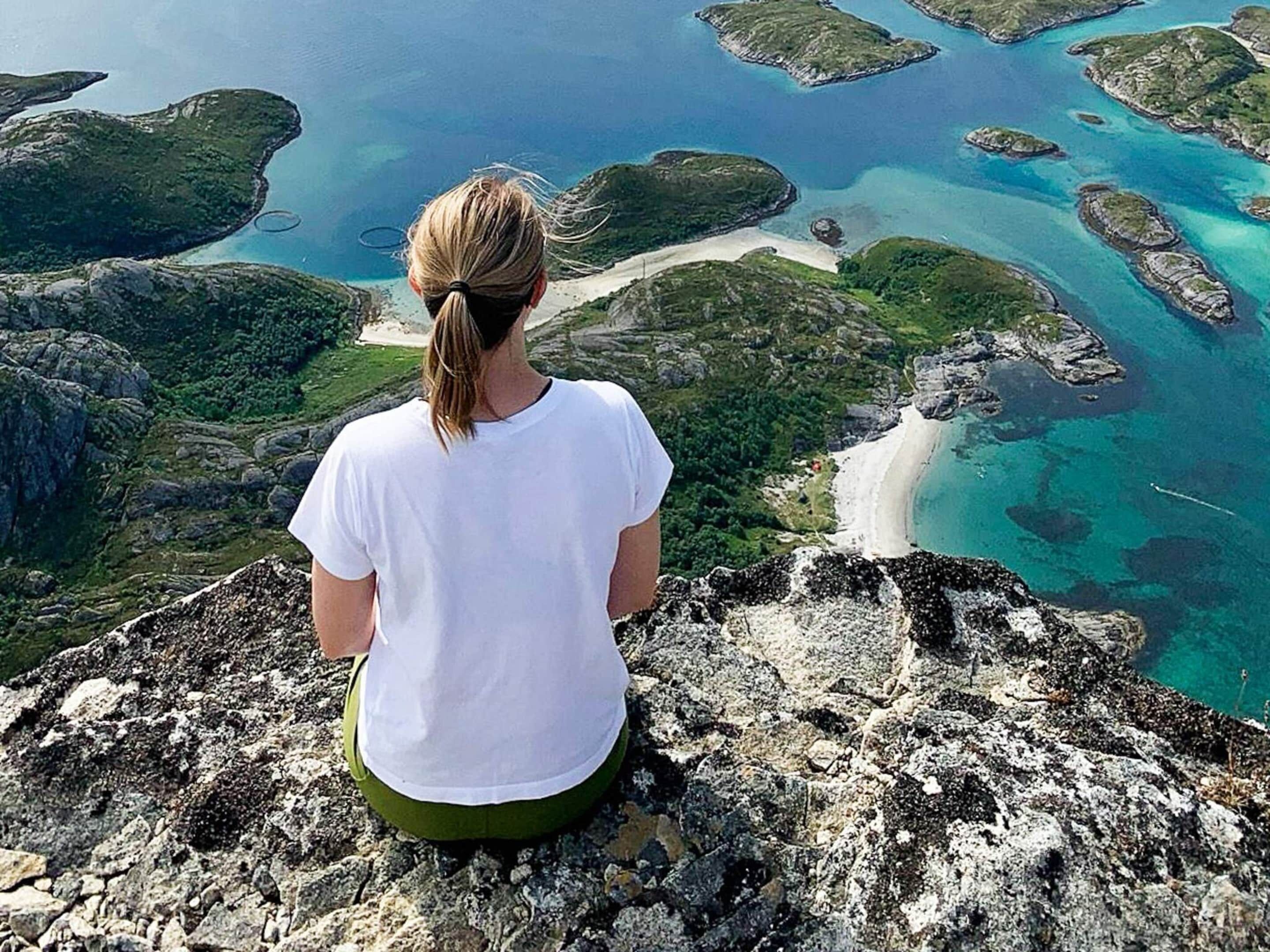 Una persona sentada sobre un afloramiento rocoso, con vistas a un paisaje costero de aguas azules cristalinas y islas verdes.