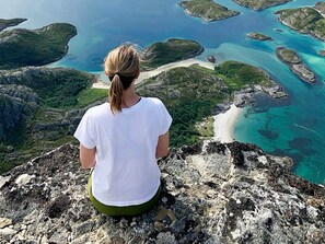 Una persona asseguda sobre una roca amb vista a un paisatge costaner d'aigües blaves cristal·lines i illes verdes.