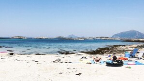 A beach with clear blue water, rocky outcrops, and distant mountains. - 4 Star Holiday Home in Vikholmen (Nesna)