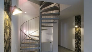 Una escalera de caracol en un pasillo con un radiador y un panel decorativo en la pared.