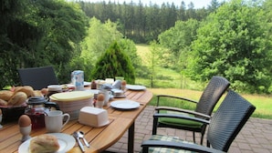 Una mesa para comer al aire libre con platos, vasos y comida, rodeada de sillas con cojines.