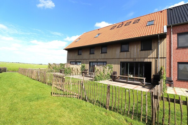 A two-story building with a red-tiled roof, a wooden facade, and a fenced outdoor area with seating. - Villa in Leons With Sloop Rentals (Leons)