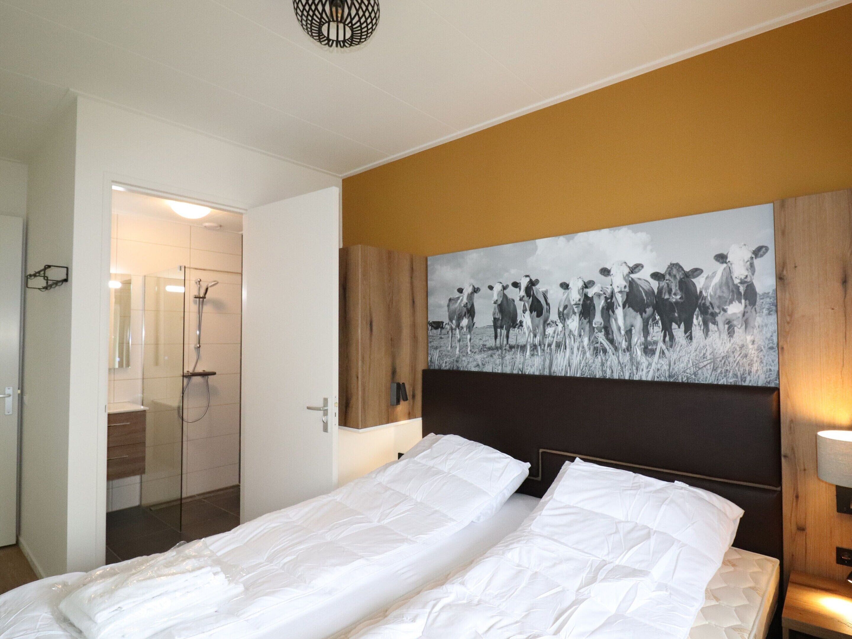 A hotel room with a bed, a shower, and a large wall-mounted picture of cows.