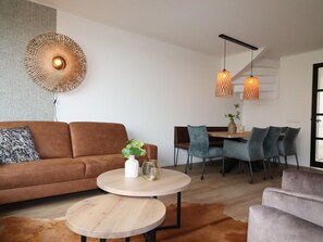 A modern living room with a brown sofa, two round wooden tables, and a dining area with blue chairs. - Villa in Leons With Sloop Rentals (Leons)