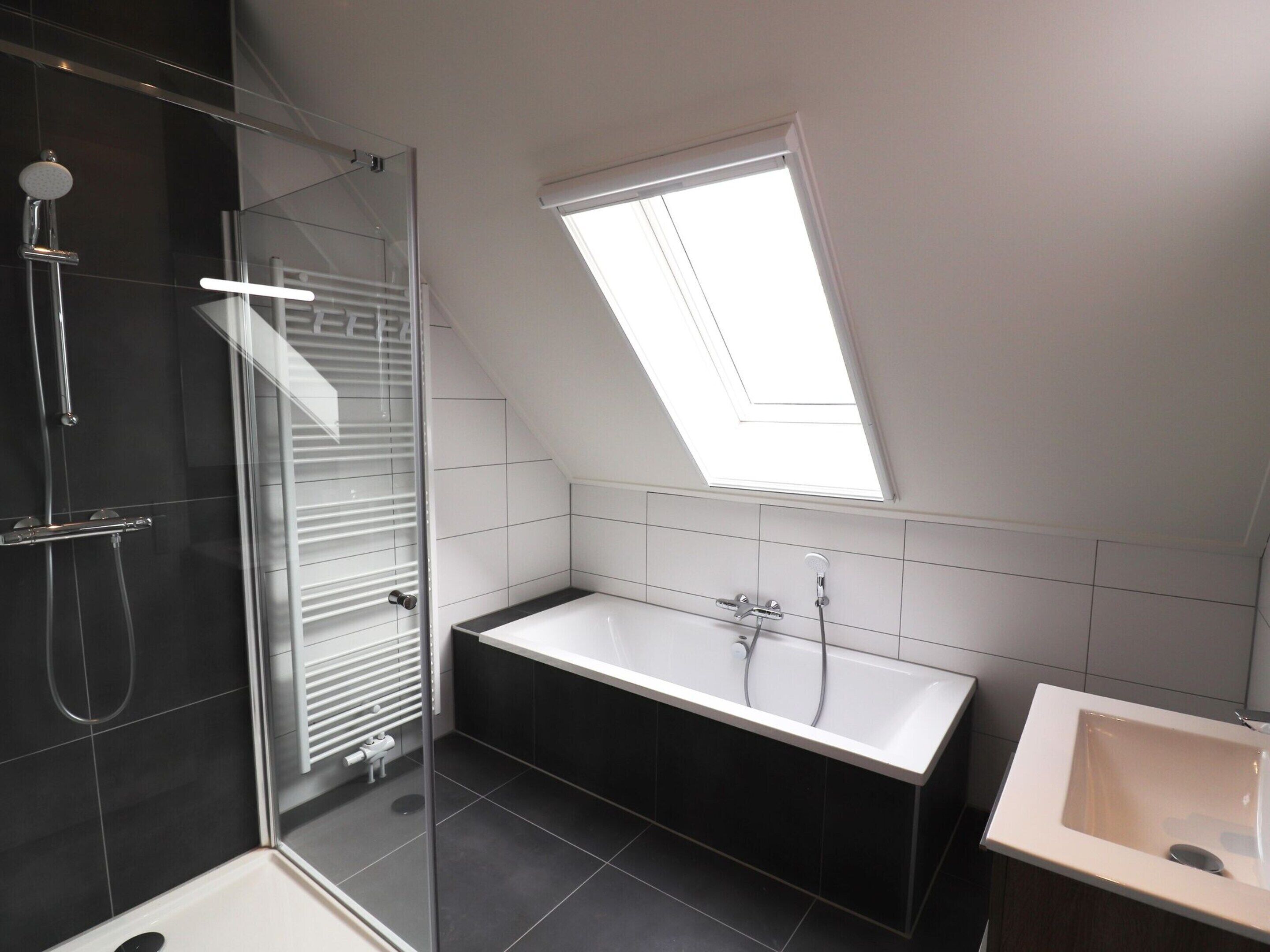 Ein modernes Badezimmer mit Duschkabine aus Glas, freistehender Badewanne und einem Fenster für natürliches Licht.