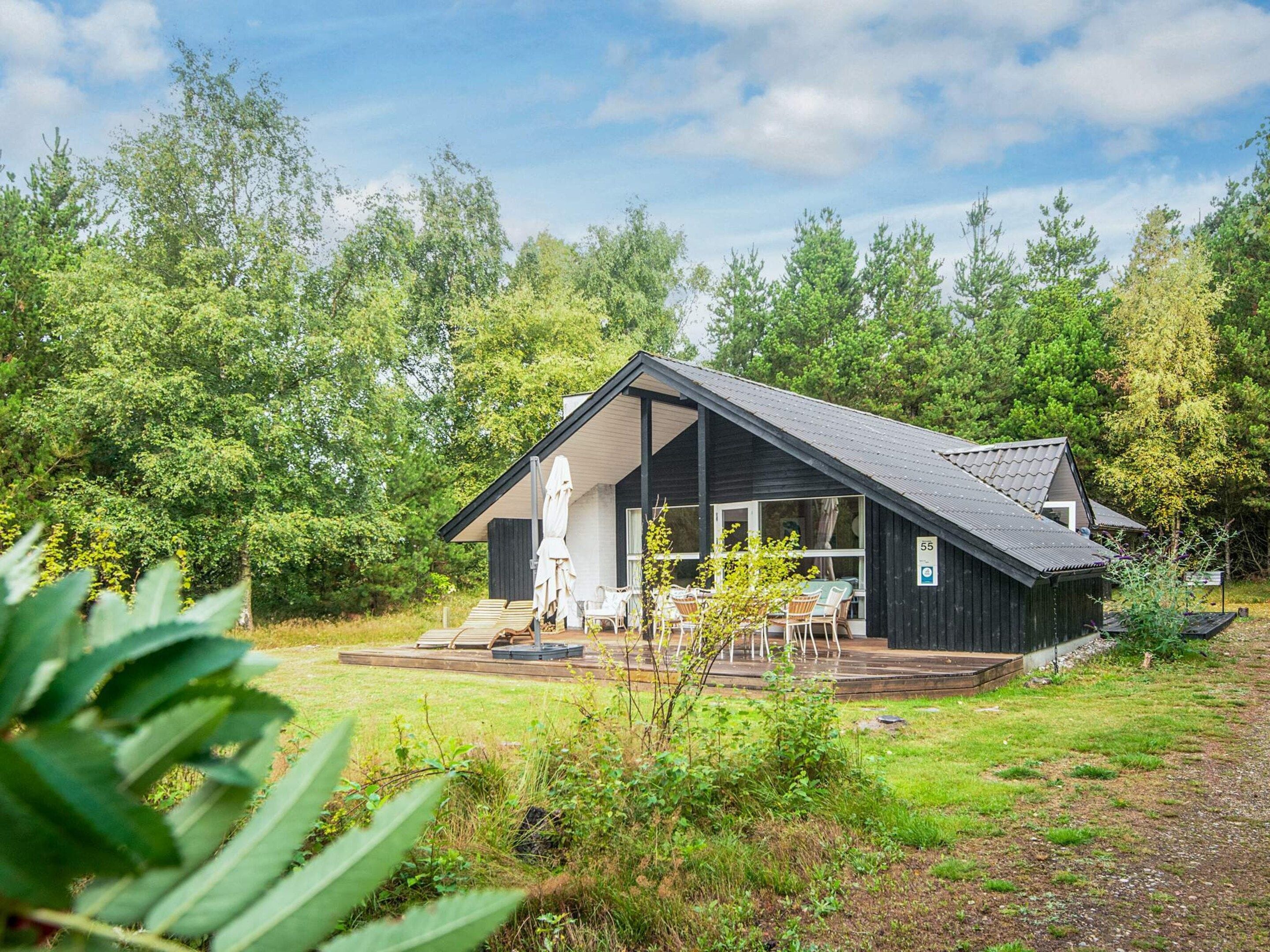 A cabin with a deck, outdoor seating, and a view of the surrounding forest.