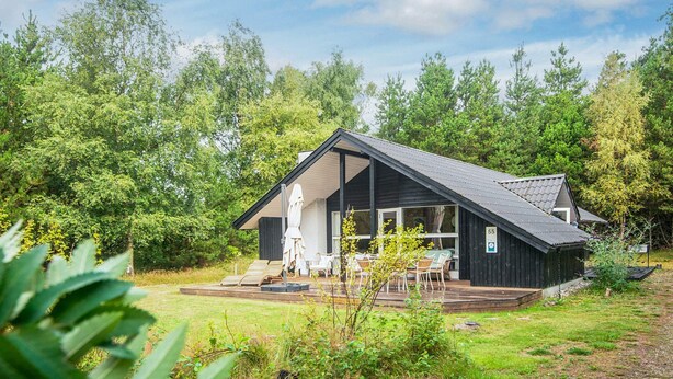 Une cabane dotée d’une terrasse, de meubles de jardin et offrant une vue sur la forêt environnante.