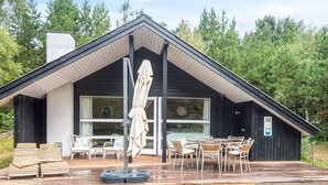 A cabin with a covered deck, outdoor seating, and a large window. - 6 Person Holiday Home in Norre Nebel (Norre Nebel)