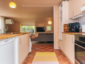 A compact kitchen with wooden cabinets, a built-in oven, and a coffee machine. - 6 Person Holiday Home in Norre Nebel (Norre Nebel)