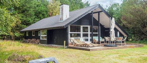 Una casa moderna con una terraza grande, mobiliario exterior y vistas al bosque circundante.