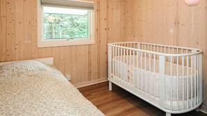 Une pièce aux murs en bois, avec un berceau, une fenêtre et un lit.
