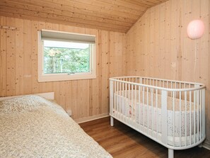 A room with wooden walls, a crib, a window, and a bed. - 6 Person Holiday Home in Norre Nebel (Norre Nebel)