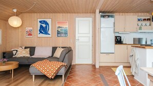 Un salon chaleureux avec un canapé, une table basse et un plaid à motifs. Il y a également un coin cuisine équipé d’un réfrigérateur, d’un évier et de placards.