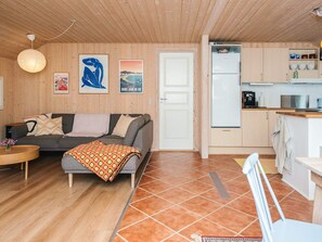 A cozy living room with a sofa, a coffee table, and a patterned throw blanket. There is a kitchen area with a refrigerator, a sink, and cabinets. - 6 Person Holiday Home in Norre Nebel (Norre Nebel)