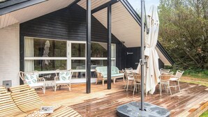 A covered outdoor seating area with wooden furniture and a table, a large window, and a view of trees. - 6 Person Holiday Home in Norre Nebel (Norre Nebel)