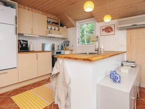 A kitchen with wooden cabinets, a stainless steel refrigerator, a coffee machine, and a window with a view of trees. - 6 Person Holiday Home in Norre Nebel (Norre Nebel)