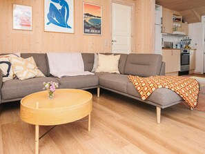 A living room with a sofa, a coffee table, and a kitchen area with cabinets and appliances. - 6 Person Holiday Home in Norre Nebel (Norre Nebel)