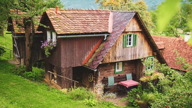 Ein rustikales Holzhaus mit geneigtem Dach, grünen Fensterläden und einer kleinen Veranda.