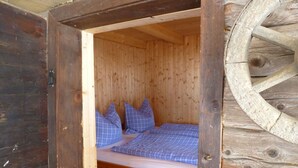 Ein hölzernes Bett mit blau-kariertem Bettzeug in einem rustikalen Zimmer mit Holzwänden und einer großen Holzradkonstruktion.