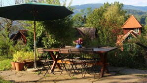 Eine Terrasse im Freien mit einem Holztisch, Stühlen, einem Sonnenschirm und Topfpflanzen.