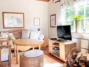 A cozy living room with a sofa, a television, a wooden table, and a wicker ottoman. - 4 Star Holiday Home in Aplared (Aplared)