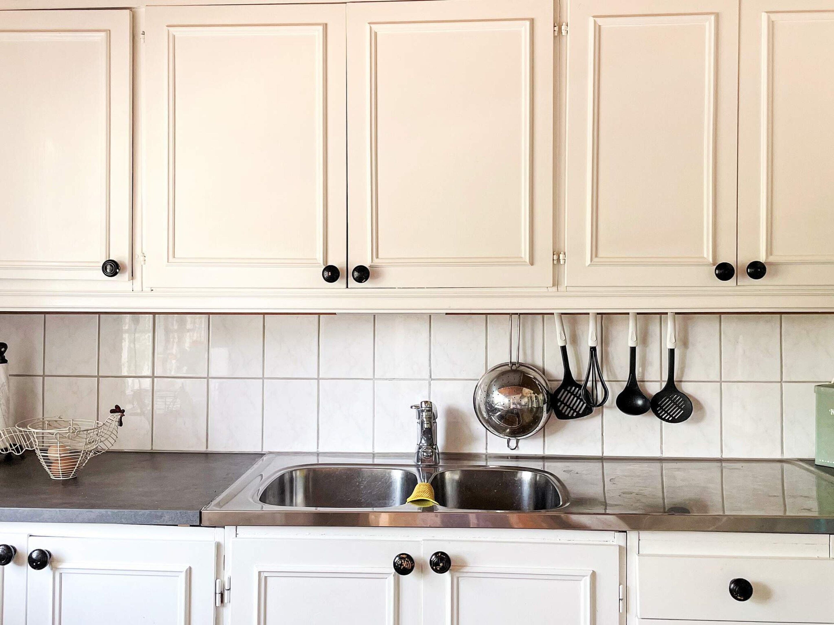 A kitchen with white cabinets, a stainless steel sink, and hanging kitchen utensils.