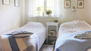 A bedroom with two single beds, a window with checkered curtains, a bedside table with a lamp, and framed pictures on the wall. - 4 Star Holiday Home in Aplared (Aplared)