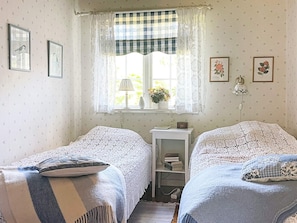A bedroom with two single beds, a window with checkered curtains, a bedside table with a lamp, and framed pictures on the wall. - 4 Star Holiday Home in Aplared (Aplared)