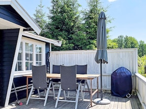 An outdoor deck with a table and chairs, a barbecue grill, and a covered umbrella. - 4 Star Holiday Home in Aplared (Aplared)