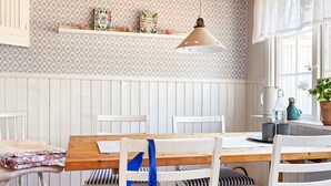 A dining area with a wooden table, white chairs, and a hanging pendant light. - 4 Star Holiday Home in Aplared (Aplared)