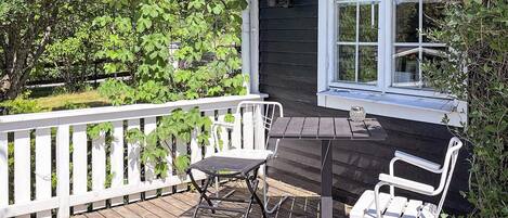 A wooden deck with a white railing, a table, and two chairs.