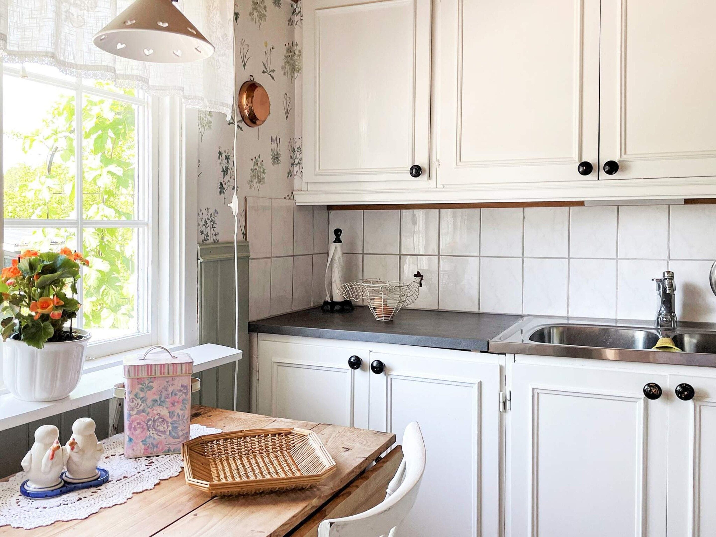 A kitchen with white cabinets, a wooden countertop, a sink, and a window with a view of greenery.