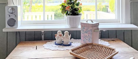 A wooden table with a wicker basket, salt and pepper shakers, a potted plant, and a speaker on a windowsill.