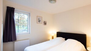 A bedroom with a bed, a window with curtains, a radiator, and wall-mounted artwork. - Pavilion 6 People XL (Zorgvlied)