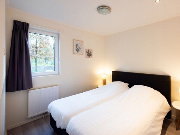 A bedroom with a bed, a window with curtains, a radiator, and wall-mounted artwork. - Pavilion 6 People XL (Zorgvlied)