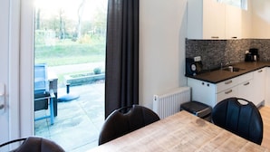 A modern kitchen with white cabinets, a black backsplash, and a window overlooking a garden. - Pavilion 6 People XL (Zorgvlied)